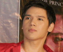 a young man in a red jacket stands in front of a poster for the prince