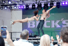 a man and a woman perform on stage in front of a brick 's logo