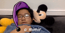 a man wearing glasses and a purple hat laying next to a mickey mouse stuffed animal