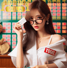 a woman wearing glasses and a white shirt with a red sticker that says ' togel ' on it