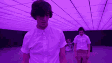 two men in white shirts are standing in a purple room .