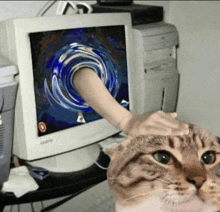 a cat is looking at a computer monitor with a hand sticking out of it