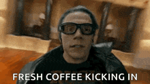 a man wearing glasses and a leather jacket is holding a cup of coffee .
