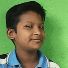 a young boy is standing in front of a green wall and smiling .