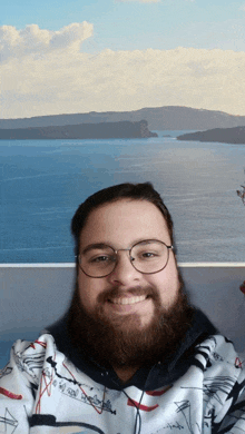 a man with a beard wearing glasses is smiling in front of a picture of the ocean