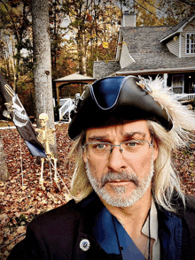 a man wearing a pirate hat stands in front of a house with a skeleton in the background