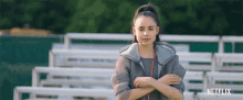 a woman stands in front of a row of bleachers with her arms crossed and a netflix logo in the corner