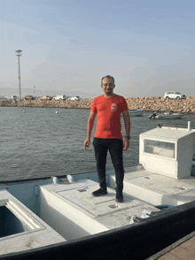 a man wearing a red shirt that says hi stands on a boat