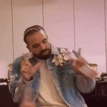 a man with a beard wearing a denim jacket is sitting on a couch holding a bottle of water .