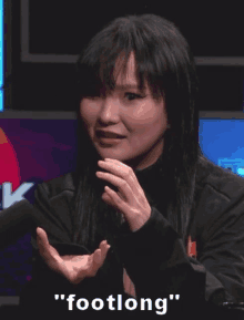 a woman is sitting in front of a microphone with her hands outstretched and a caption that says footlong .