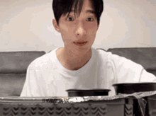 a young man in a white shirt is sitting on a couch with a tray of food in front of him .