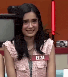 a young woman wearing a pink top with the name eliza on it is smiling .