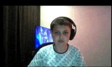 a boy wearing headphones looks at the camera with a tv in the background