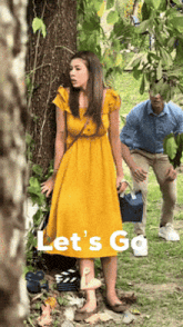 a woman in a yellow dress stands next to a tree with the words let 's go written on the bottom