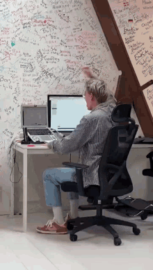 a man sits at a desk with a laptop in front of a wall that has graffiti on it including the name camelle