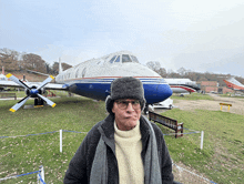 a man wearing a hat stands in front of a large airplane