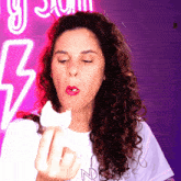 a woman with curly hair is eating a piece of cake in front of a neon sign that says nyc