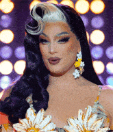 a drag queen is wearing a dress with flowers on it and earrings with flowers on them .