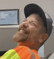 a man wearing an orange vest and a hat is smiling .