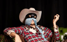 a man wearing a mask and a cowboy hat sits on a couch