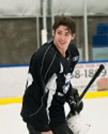 a young man is holding a hockey stick on the ice and smiling .