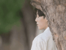 a man in a white shirt is leaning against a tree with his eyes closed