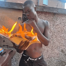 a shirtless man wearing nike shorts holds a burning book