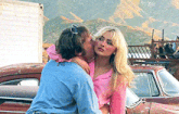 a man kisses a woman on the cheek in front of a red car