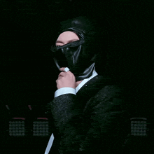 a man in a black suit is wearing a black hood over his head .