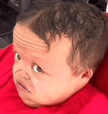 a baby is making a funny face while sitting in a red shirt .