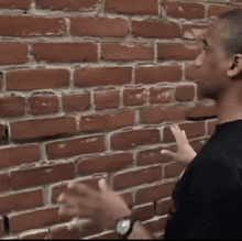 a man wearing a watch is standing in front of a red brick wall