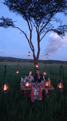 a man and a woman sit at a table with lanterns hanging from a tree