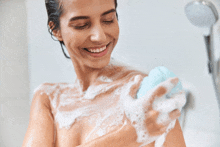 a woman is taking a shower and smiling while holding a soap bar