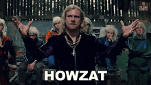 a man stands in front of a group of people with the word howzat on the bottom right