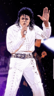 a man in a white outfit is singing into a microphone with his hand in the air