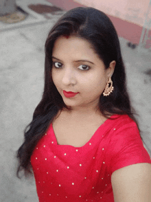 a woman wearing a red top and gold earrings is taking a selfie