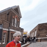 a man in a red jacket is walking down a street in front of a brick building .