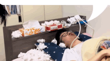 a man is laying on a bed with a box of tissues behind him