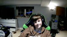 a boy wearing headphones and a hoodie that says drill cheese sits in a chair