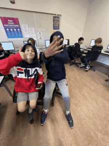 a boy wearing a fila sweatshirt is giving a thumbs up in a classroom