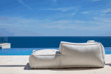 a white bean bag chair sits in front of a pool overlooking the ocean