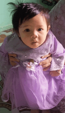 a little girl in a purple dress is being held