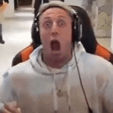 a man wearing headphones is sitting in a gaming chair with his mouth open .