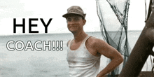 a man in a tank top stands in front of a sign that says " hey coach "