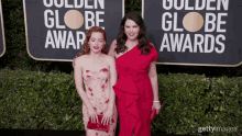 two women are posing for a picture on a red carpet in front of a sign that says golden globe awards