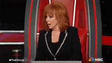 a woman with red hair is sitting in a chair with the nbc logo on the bottom