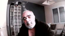 a man smoking a cigarette in front of a bookshelf