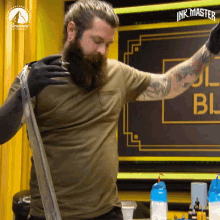 a man with a beard and tattoos is standing in front of a sign that says ink master