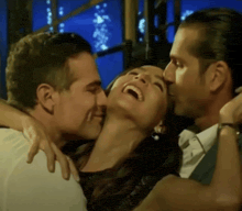 a man kisses a woman on the cheek while another man hugs her