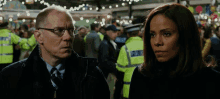 a man and a woman are standing next to each other in a crowd with a man wearing a yellow vest that says police